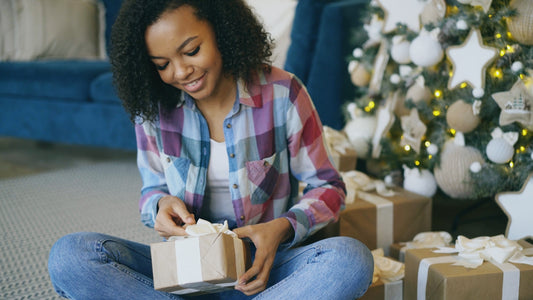 Young woman opening a christmas gift by the tree.