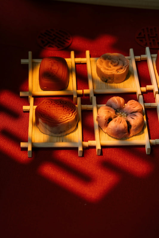 Four mooncakes arranged on bamboo mats on red background.