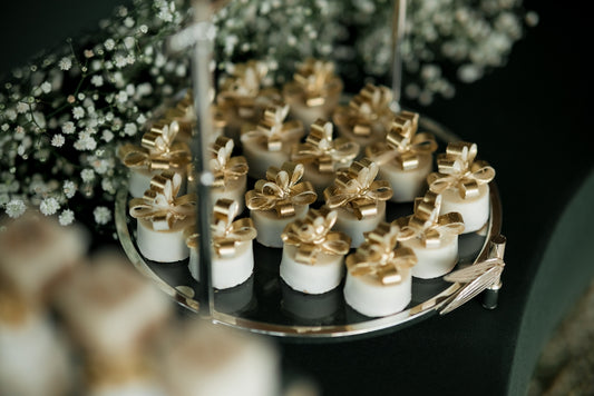 Small white desserts with gold bows on a tiered stand.