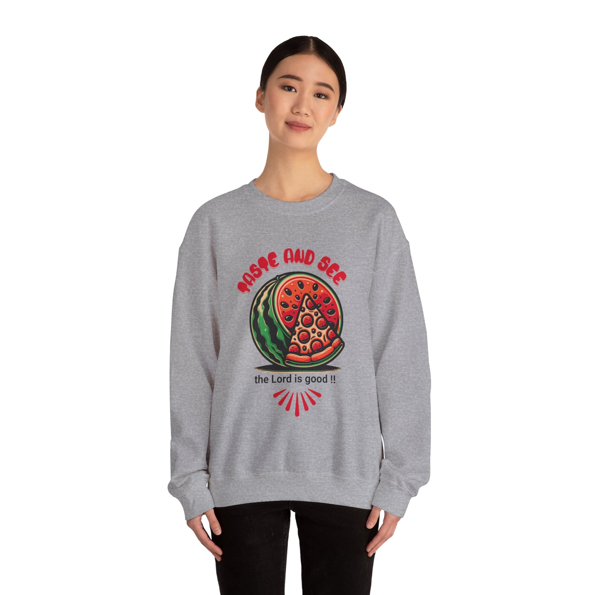 Model wearing gray crewneck jumper with Christian message 'Taste and See the Lord is Good' and bold food-themed artwork. Comfortable religious wear.